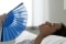 Une femme équipée d'un ventilateur réfléchit à la possibilité d'installer un système de climatisation.